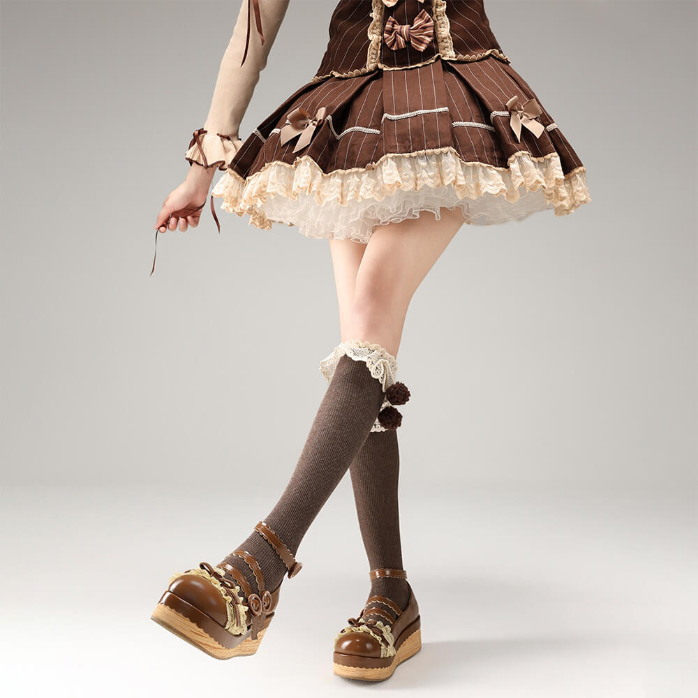 Person wearing a brown pinstripe dress with lace details, knee-high socks, and brown shoes on a gray background.