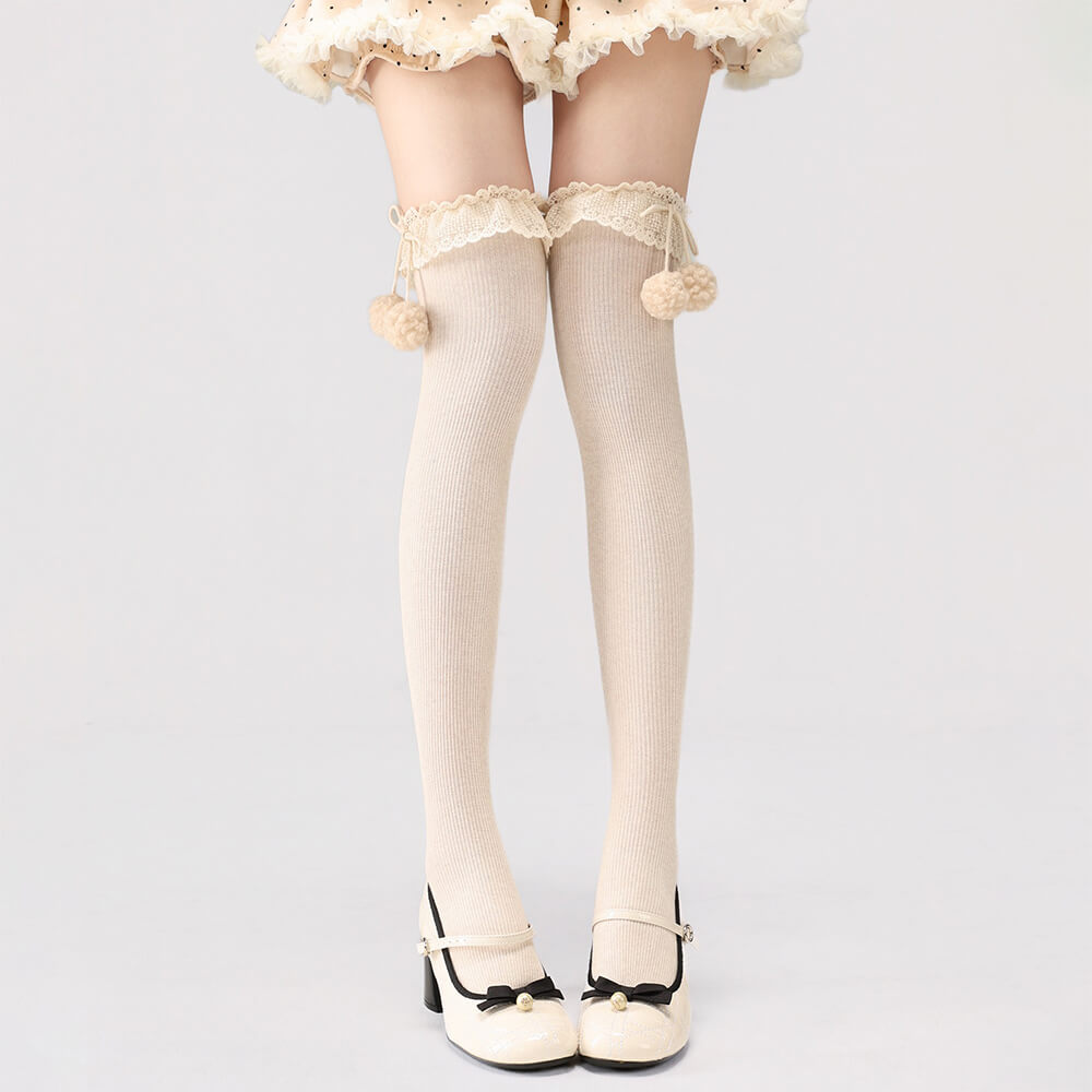Apricot lace-up stockings with pom-pom details on a plain background