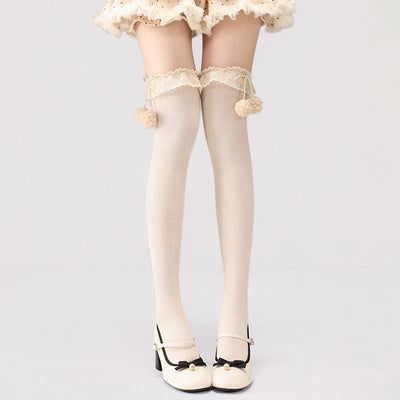 Apricot lace-up stockings with pom-pom details on a plain background