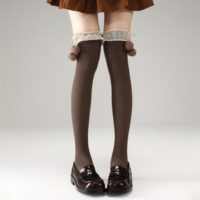 Brown knee-high socks with lace and pom-pom details worn by a person on a plain background