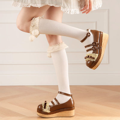 Brown shoes with decorative laces worn with white knee-high socks on a light wooden floor.