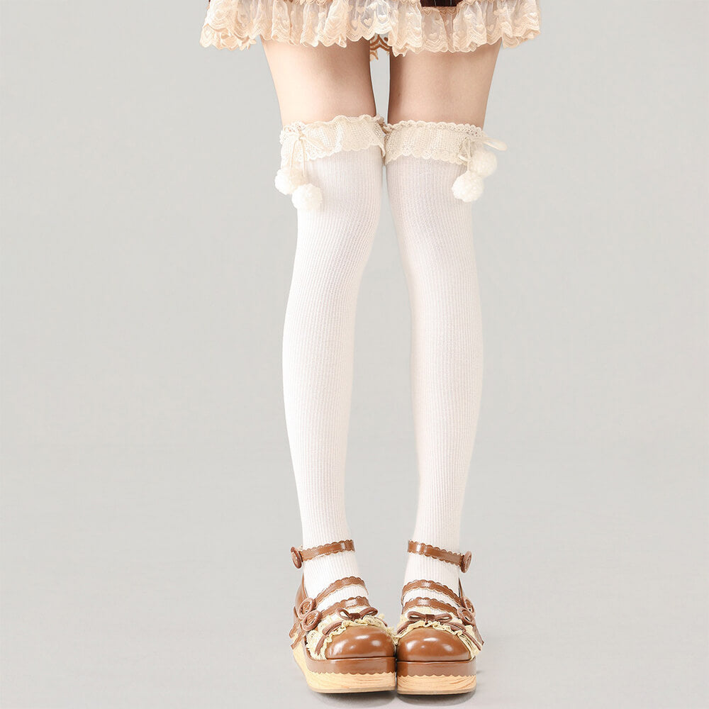 White knee-high socks with lace details worn with brown sandals on a gray background