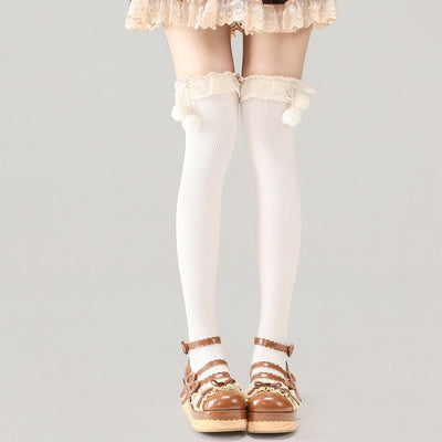 White knee-high socks with lace details worn with brown sandals on a gray background