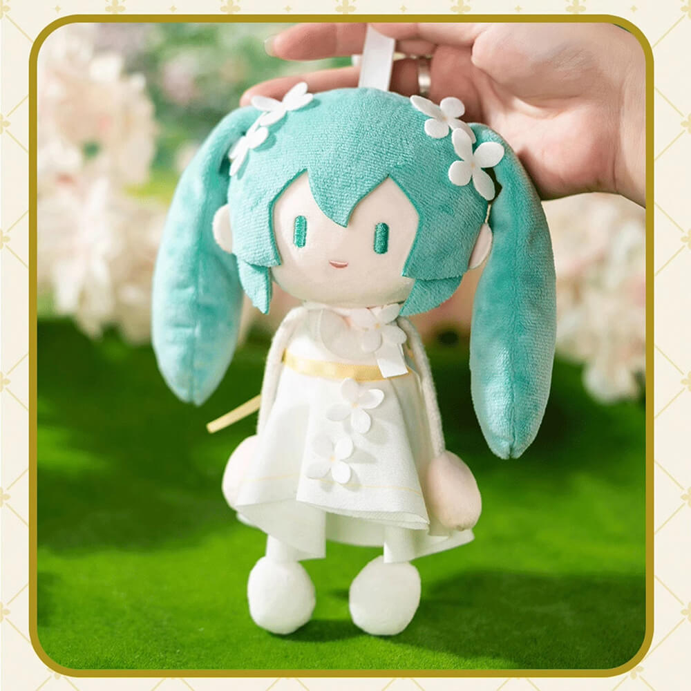 Plush Miku with teal hair and white outfit held by a hand against a blurred floral background