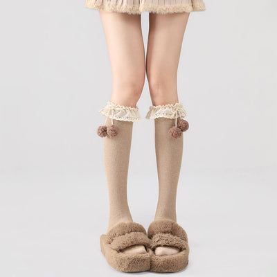Khaki below knee socks with lace and pom-pom details worn with brown slippers on a light gray background.