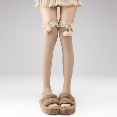Khaki thigh-high socks with lace and pom-poms worn with a skirt and brown slippers on a gray background