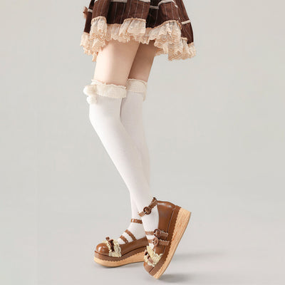 White knee-high socks with lace top worn with brown sandals on a plain background