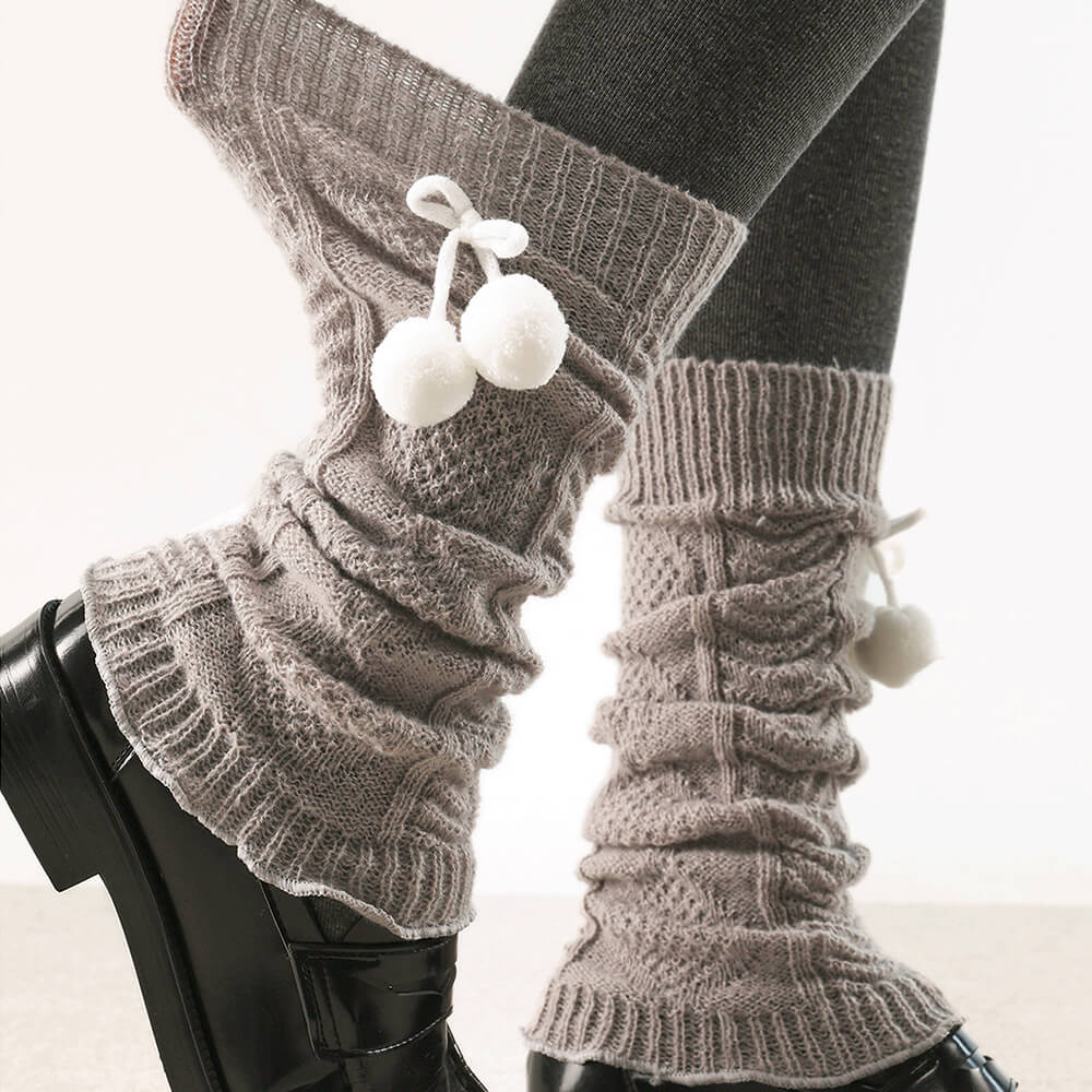 Gray knitted leg warmers with white pom-poms worn over black leggings and shoes.
